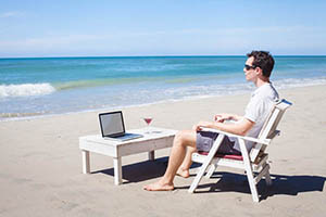 man working on laptop computer from the beach
